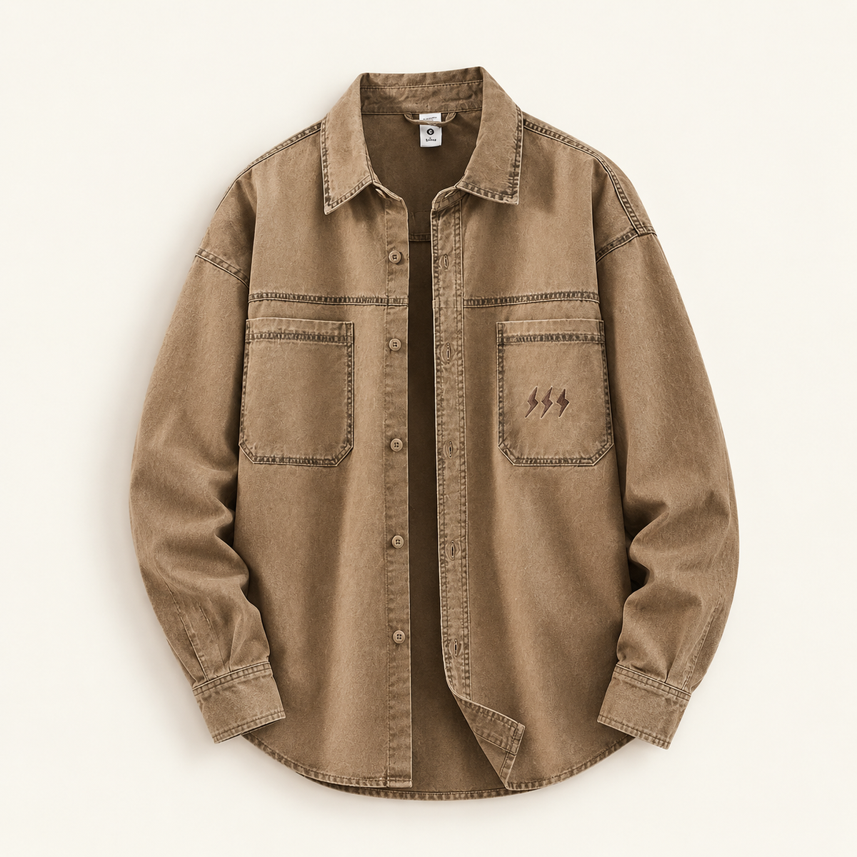 A brown washed denim button-up shirt with three-quarter sleeves, featuring two chest pockets with contrast stitching and a small embroidered lightning-bolt motif on the right pocket, displayed flat against a light cream background.