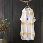 Yellow and white checkered shirt hanging on a dark wooden wall with a plant in the corner.